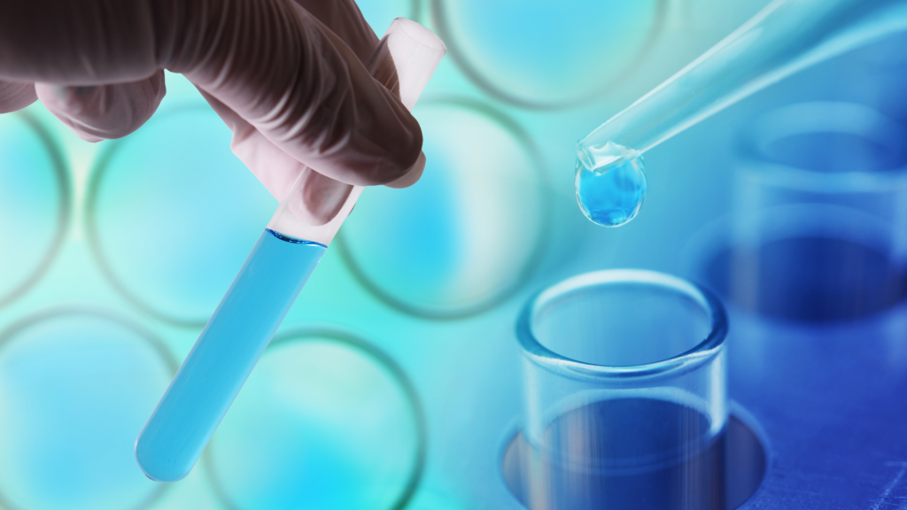 A gloved hand holds a test tube filled with blue liquid as a pipette dispenses a drop into another, symbolizing precision and care—values at the core of Marnoa Private Wealth Counsel’s financial planning expertise. Circular laboratory containers blur in the background.